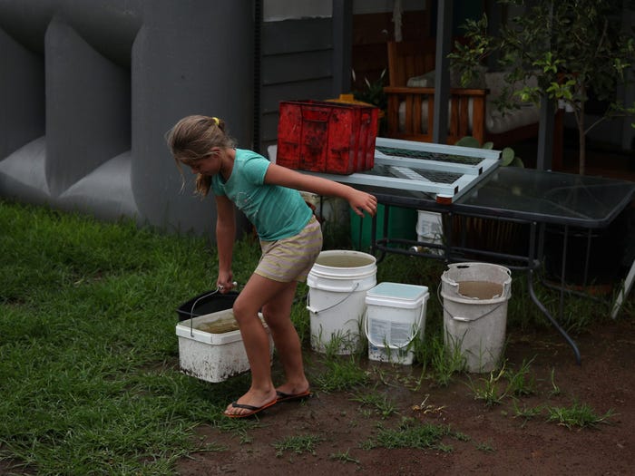 young girl carries bucket of water from a lineup of full buckets